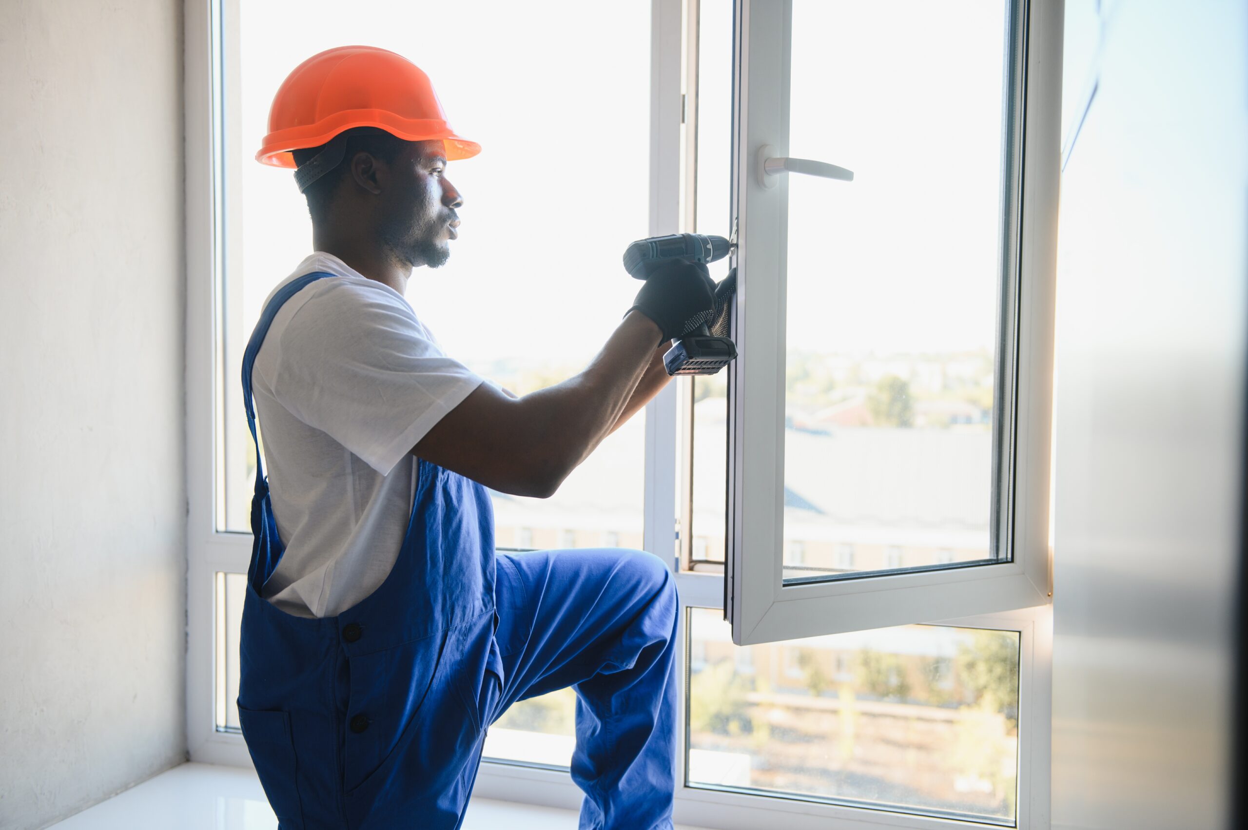 Workman in overalls installing or adjusting plastic windows in the living room at home.